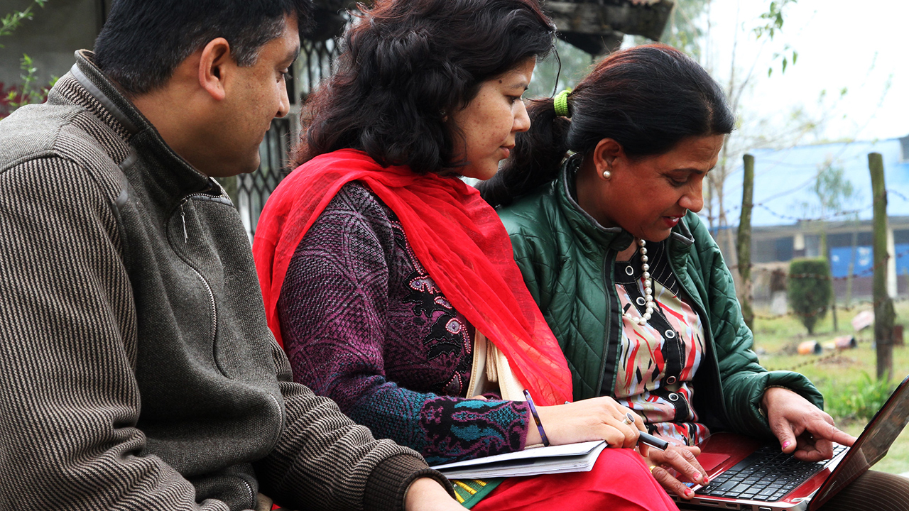 Mies ja kaksi naista katsovat tietokoneen näyttöä Nepalissa.