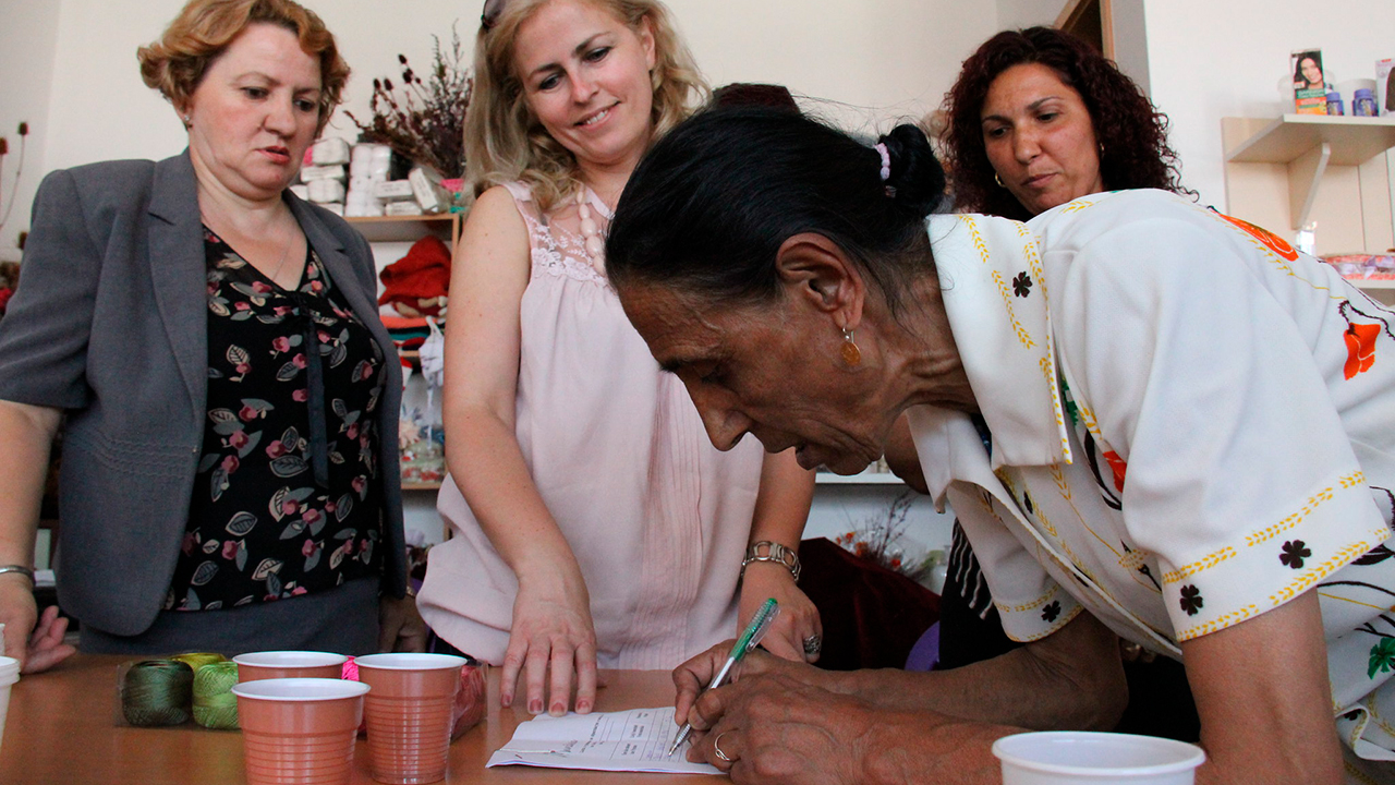 A Kosovan woman writing on a paper with hosts of Mundesia organisation.