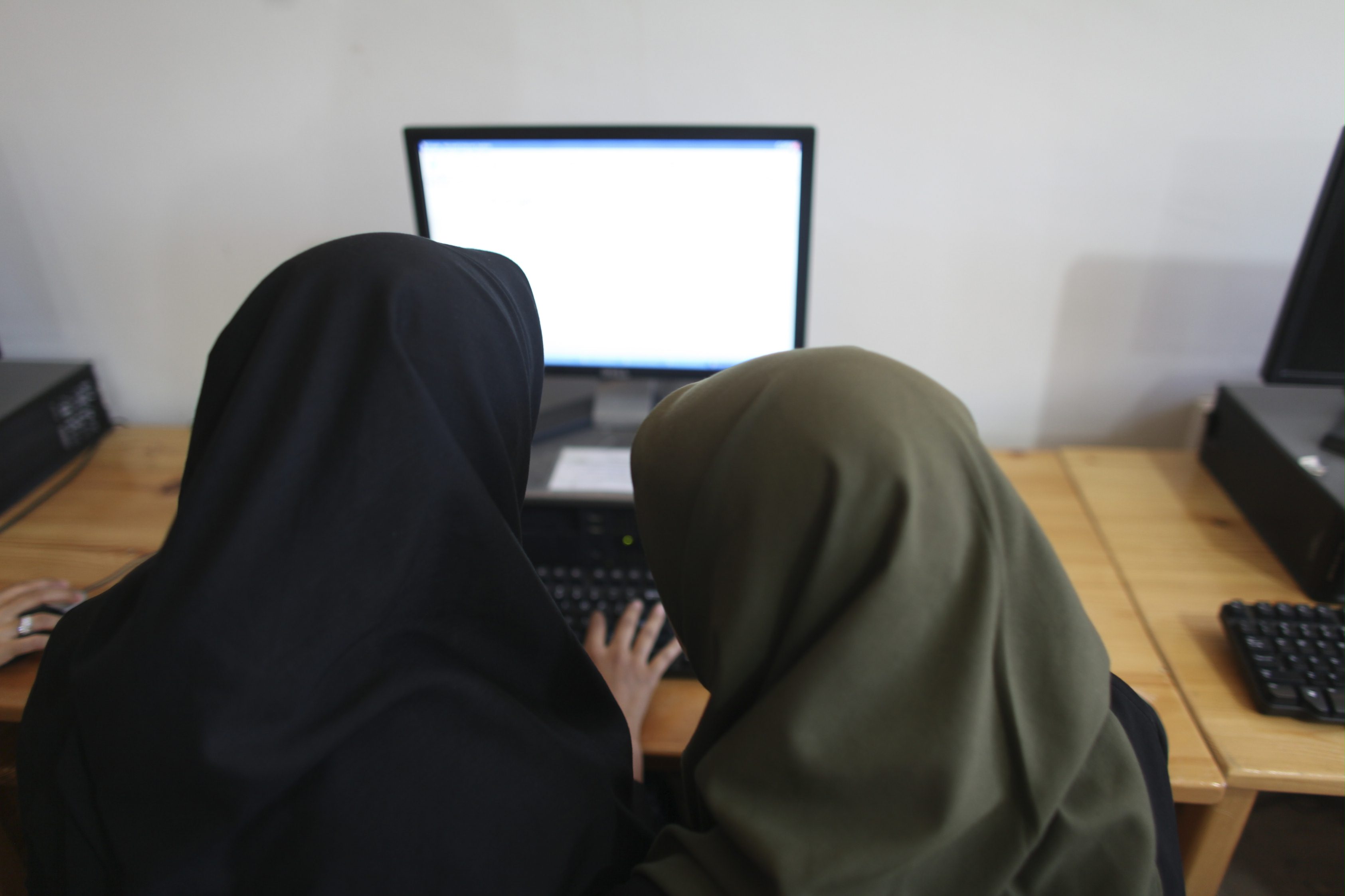 Two persons are facing a computer screen. They are wearing long scarfs.