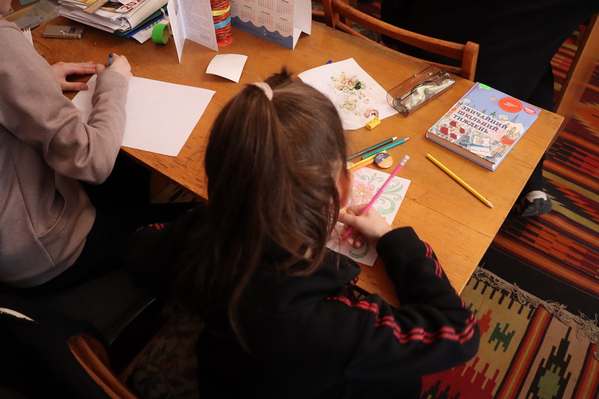 Ukrainalaistyttö värittää pöydän ääressä toisen lapsen kanssa.