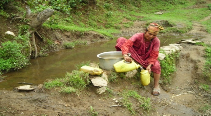Nainen istuu pienen lammikon reunalla ja kaataa kannusta astiaan vettä.