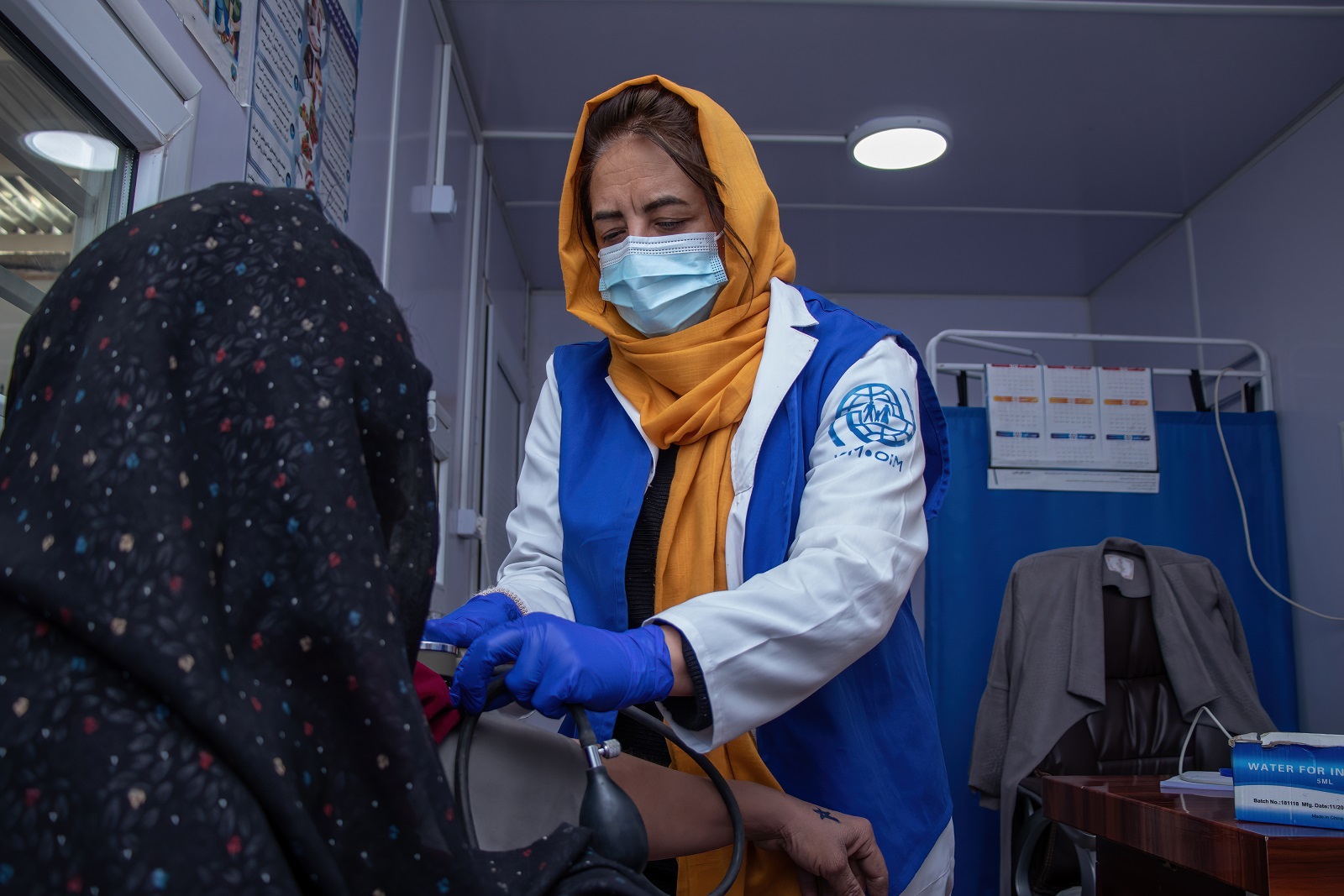 En läkare som är klädd i en jacka med symbolen för Internationella organisationen för migration mäter den afghanska kvinnans blodtryck.