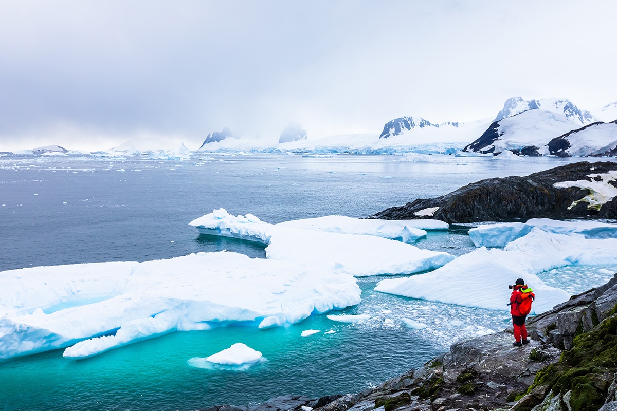 Jäävuoria, merta, kuvan laidassa ihminen retkeiluvarusteissa.