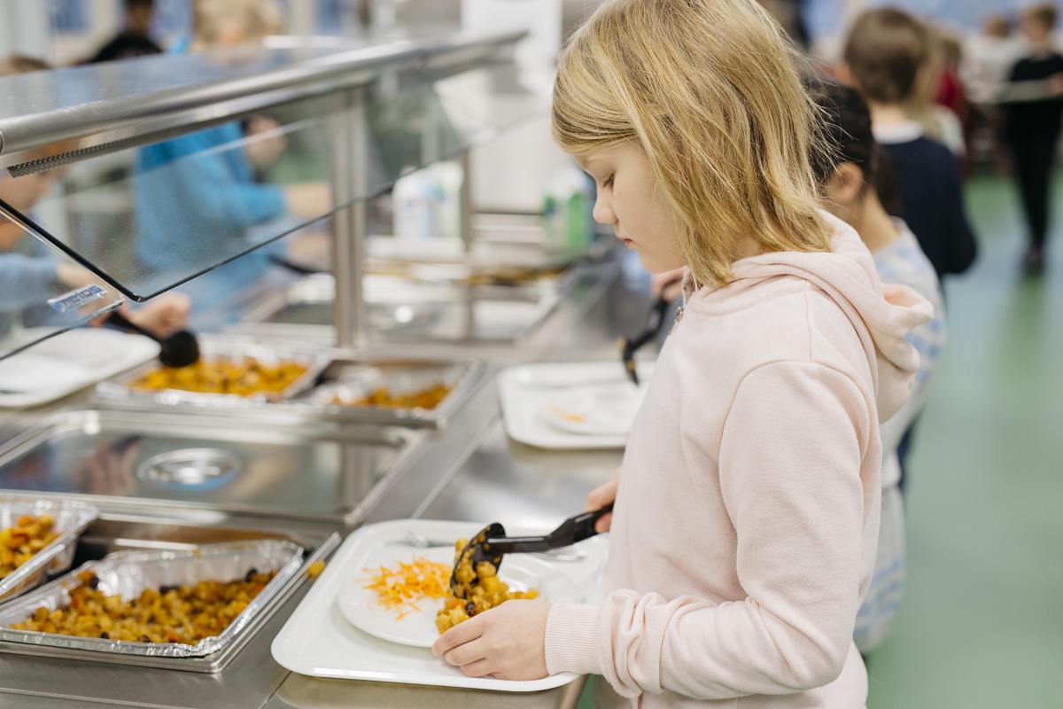 En flicka tar mat i skolmatsalen.