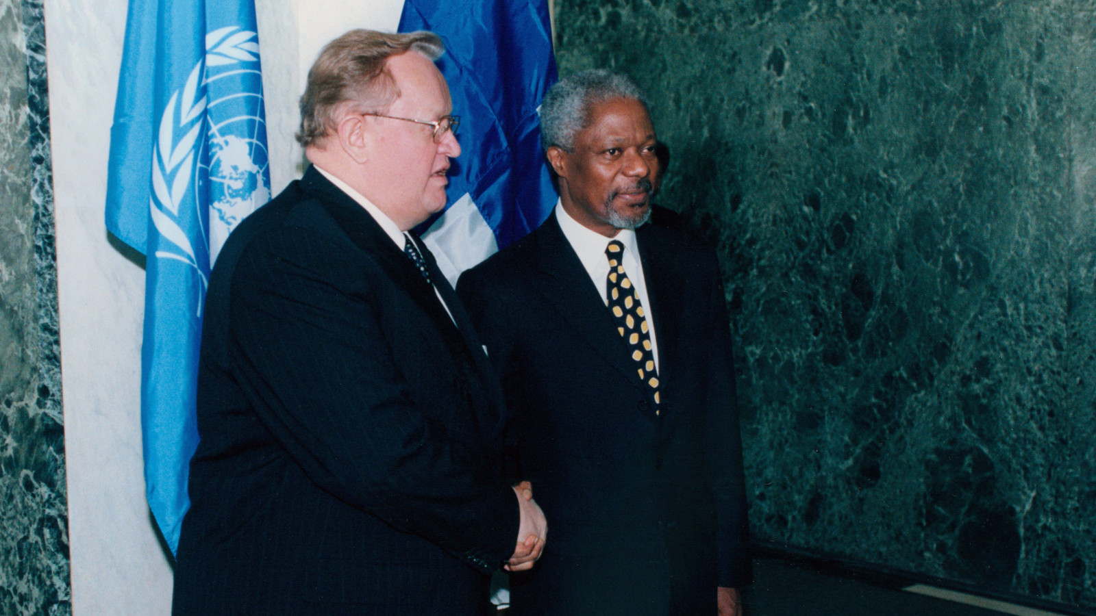 Ahtisaari kättelee Kofi Annania YK:n ja Suomen lippujen edessä.