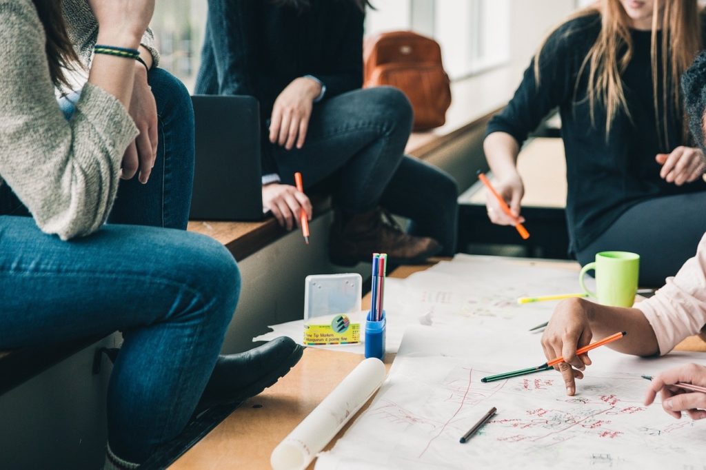 Students whose heads are not visible, planning at the table. There are pen pads and a cup of coffee on the table.