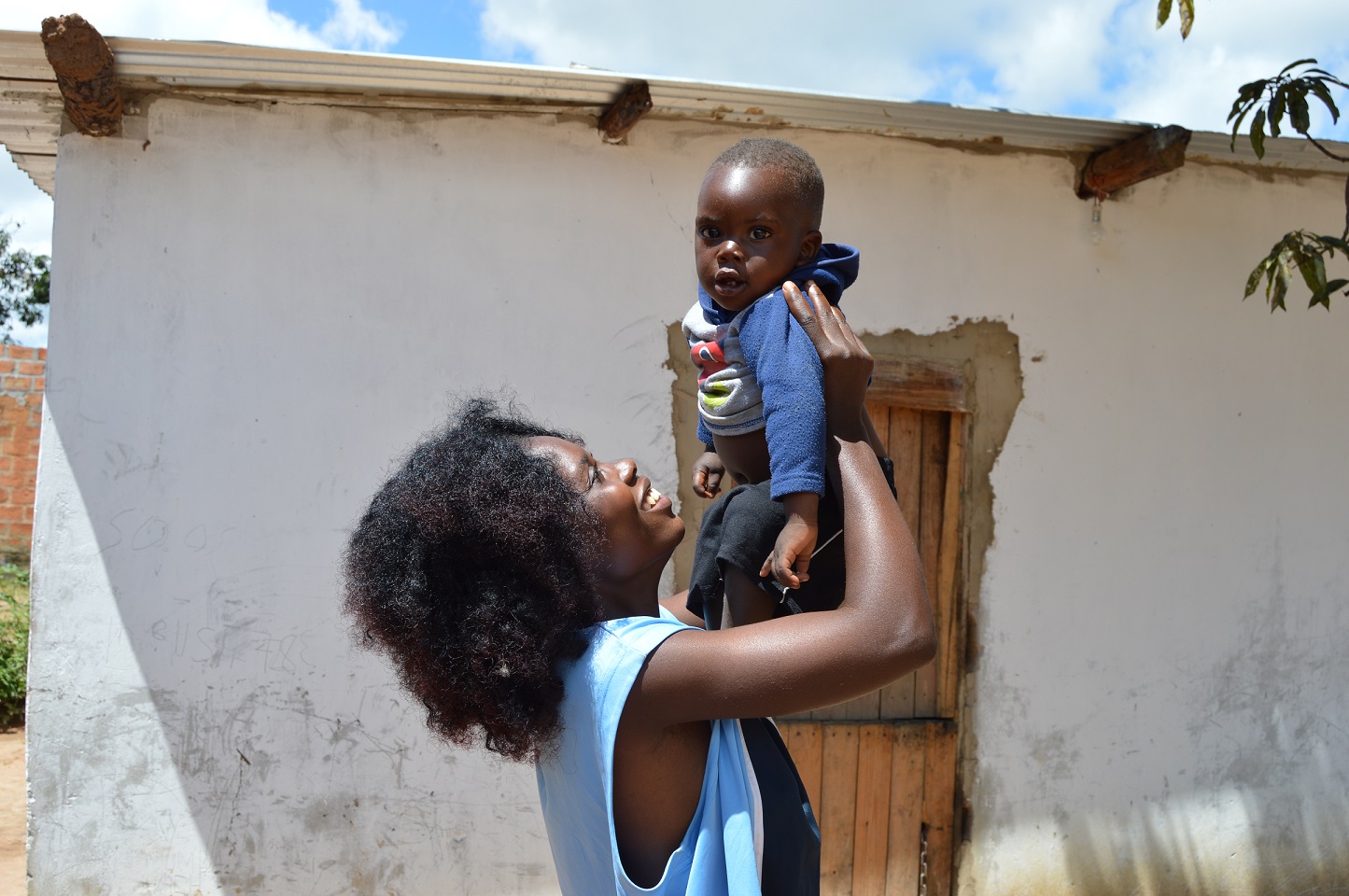 Nuori sambialainen hymyilevä nainen nostaa käsillään pientä lasta ilmaan.