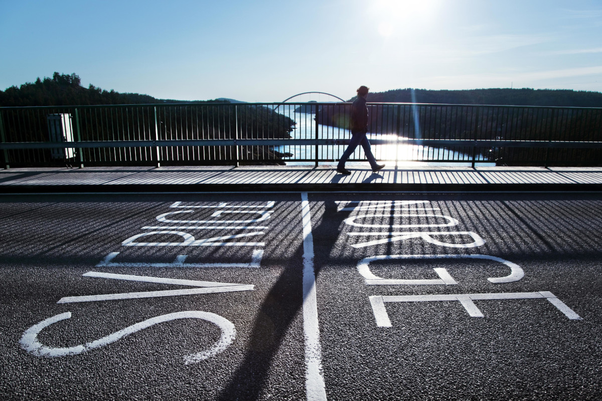 En person går längs en bro som korsar en flod. Text på bron: Sverige-Norge.