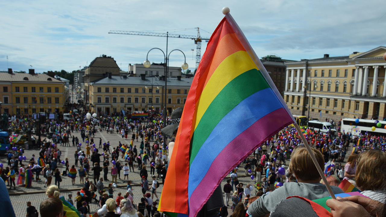 En hand håller en regnbågsflagga på Senattorget i Helsingfors.