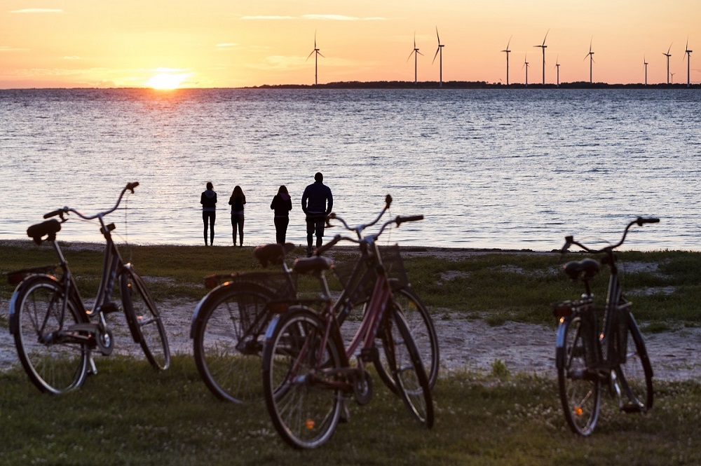 Kuvassa polkupyöriä ja ihmisiä meren rannalla. Taustalla näkyy tuulivoimala.