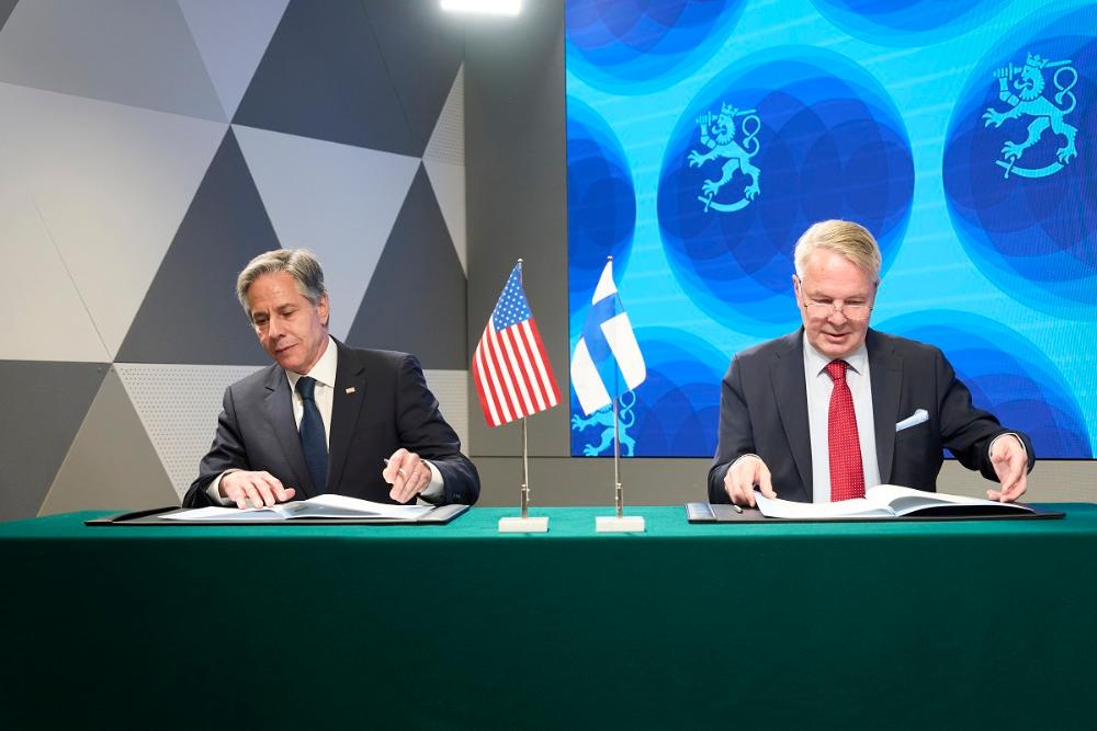 Kuvassa vasemmalla USAn ulkoministeri Blinken ja oikealla ulkoministeri Pekka Haavisto. Molemmat istuvat pöydän ääressä kansiot edessään, käsissään kynä. Keskellä USAn ja Suomen pöytäliput.