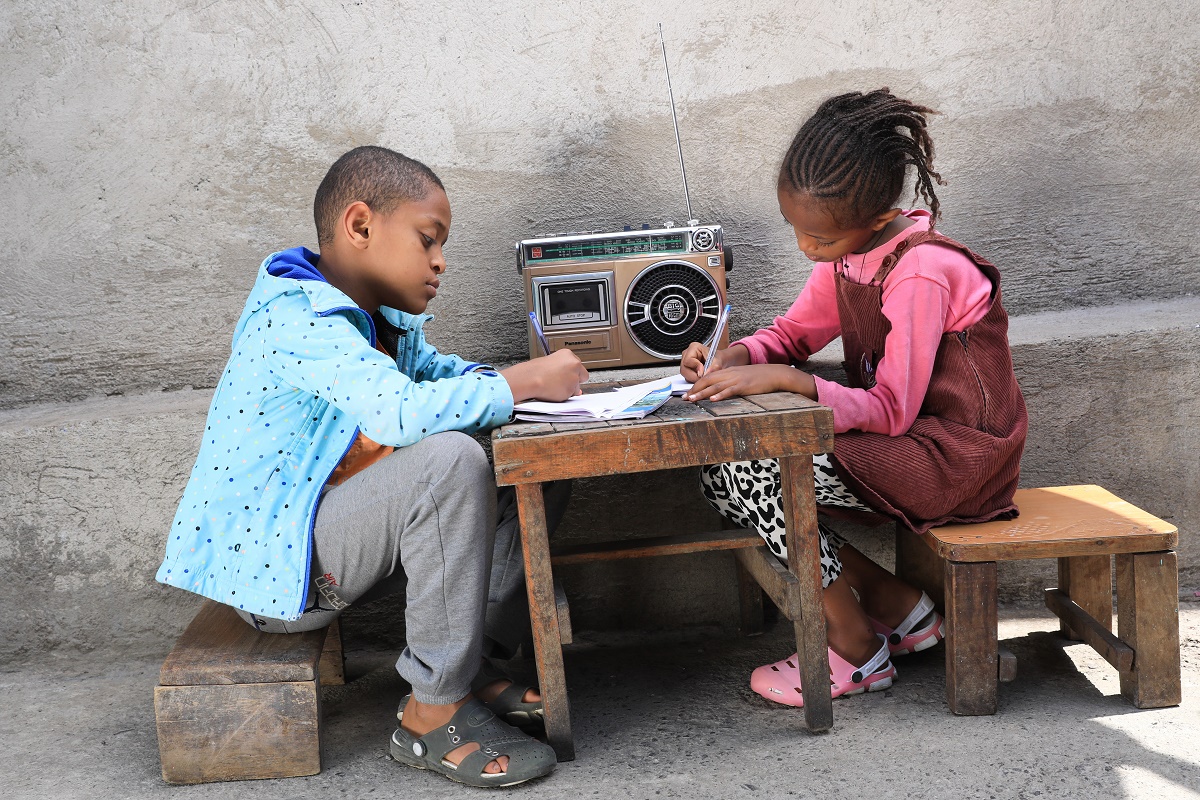 Två etiopiska barn sitter vid ett bord, lyssnar på radio och skriver i ett häfte. 