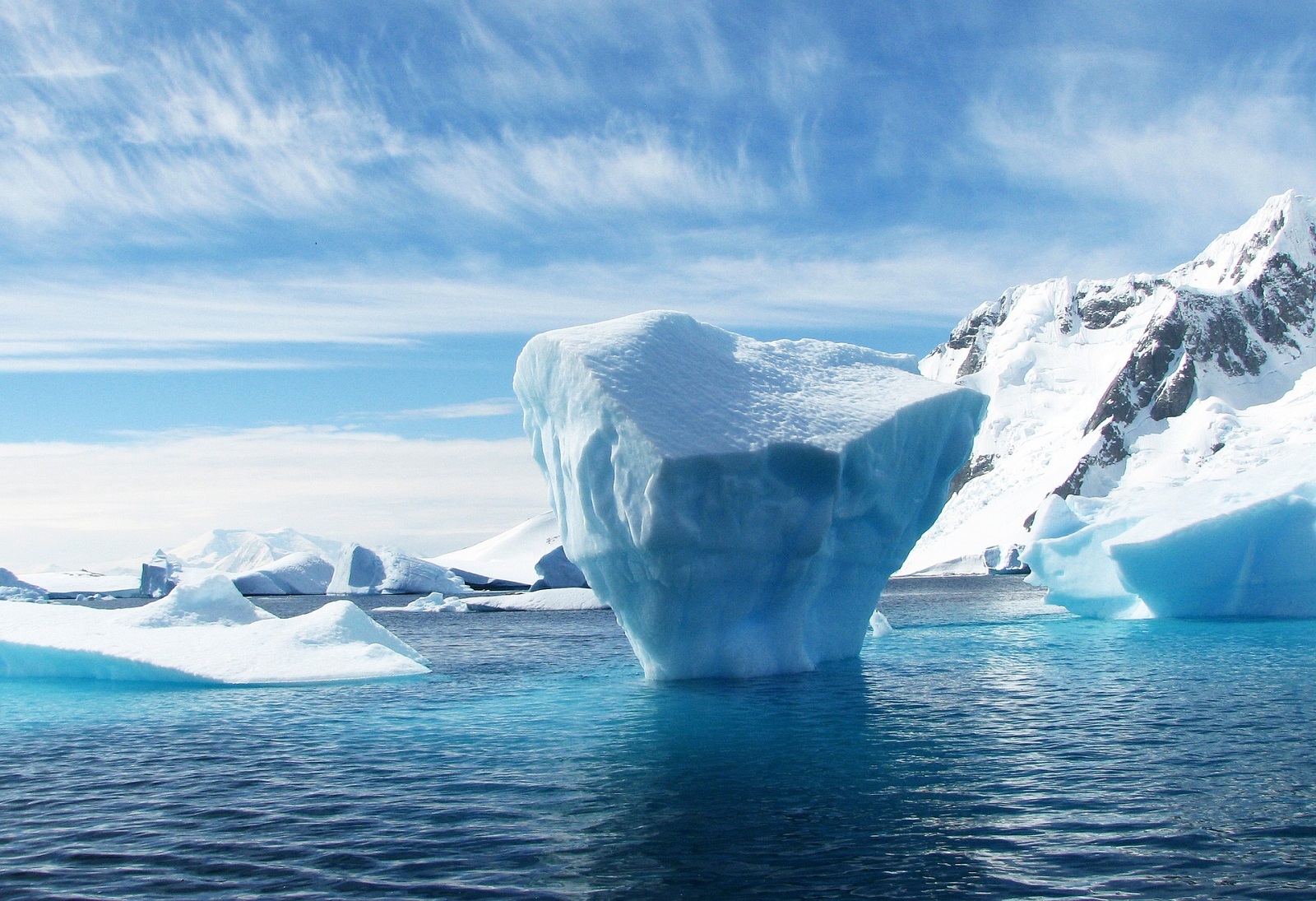 Jäävuori, etualalla suuri jäälohkare, sinistä merta. Kuva: Pixabay