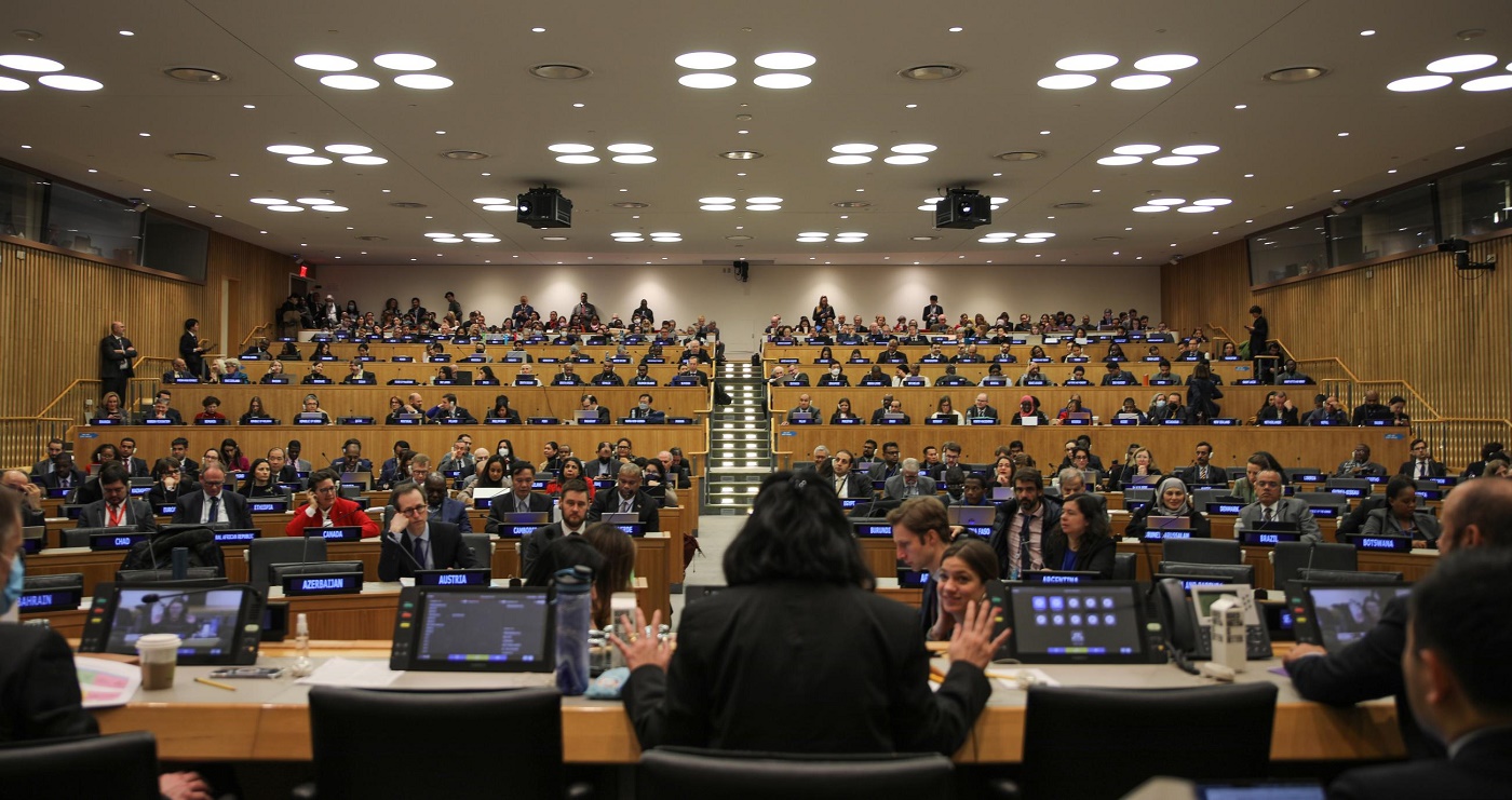 Kuva YK-kokoussalista, joka täynnä ihmisiä. Edessä puheenjohtaja, joka kuvattu selin kameraan.