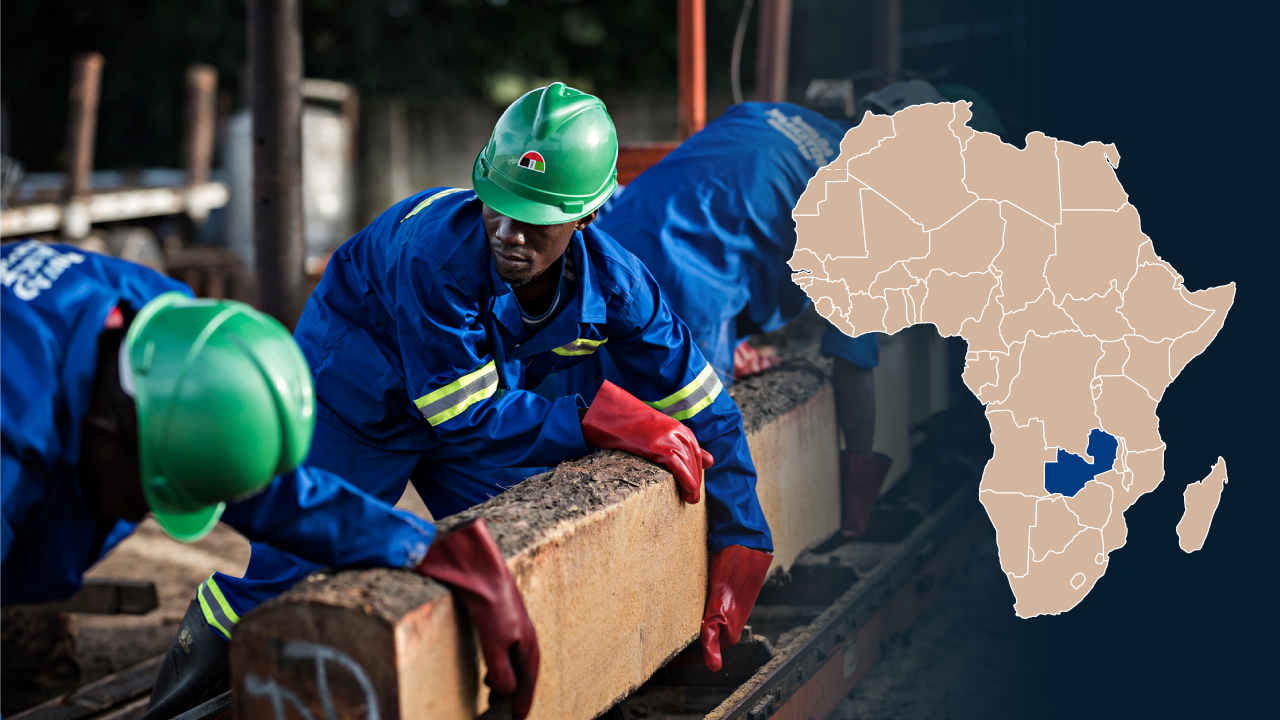 Sambialaisia rakennusmiehiä kypärät päässä. Vieressä Afrikan kartta, johon Sambia on merkitty.