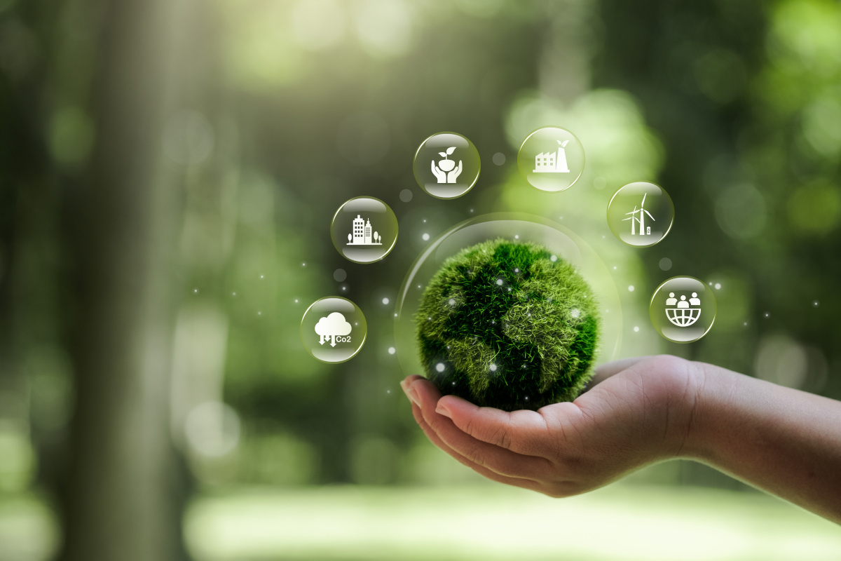 Grön jordglob i handen. Runt globen finns grafiska ikoner som beskriver hållbar utveckling och samhället.