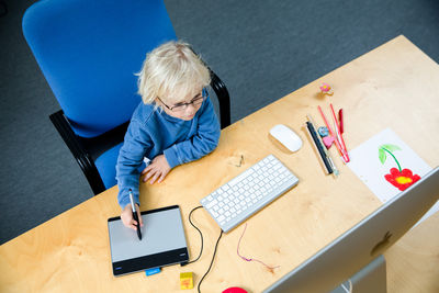 Kouluikäinen poika käyttää digitaalista piirrustuslaitetta pöydän ääressä.