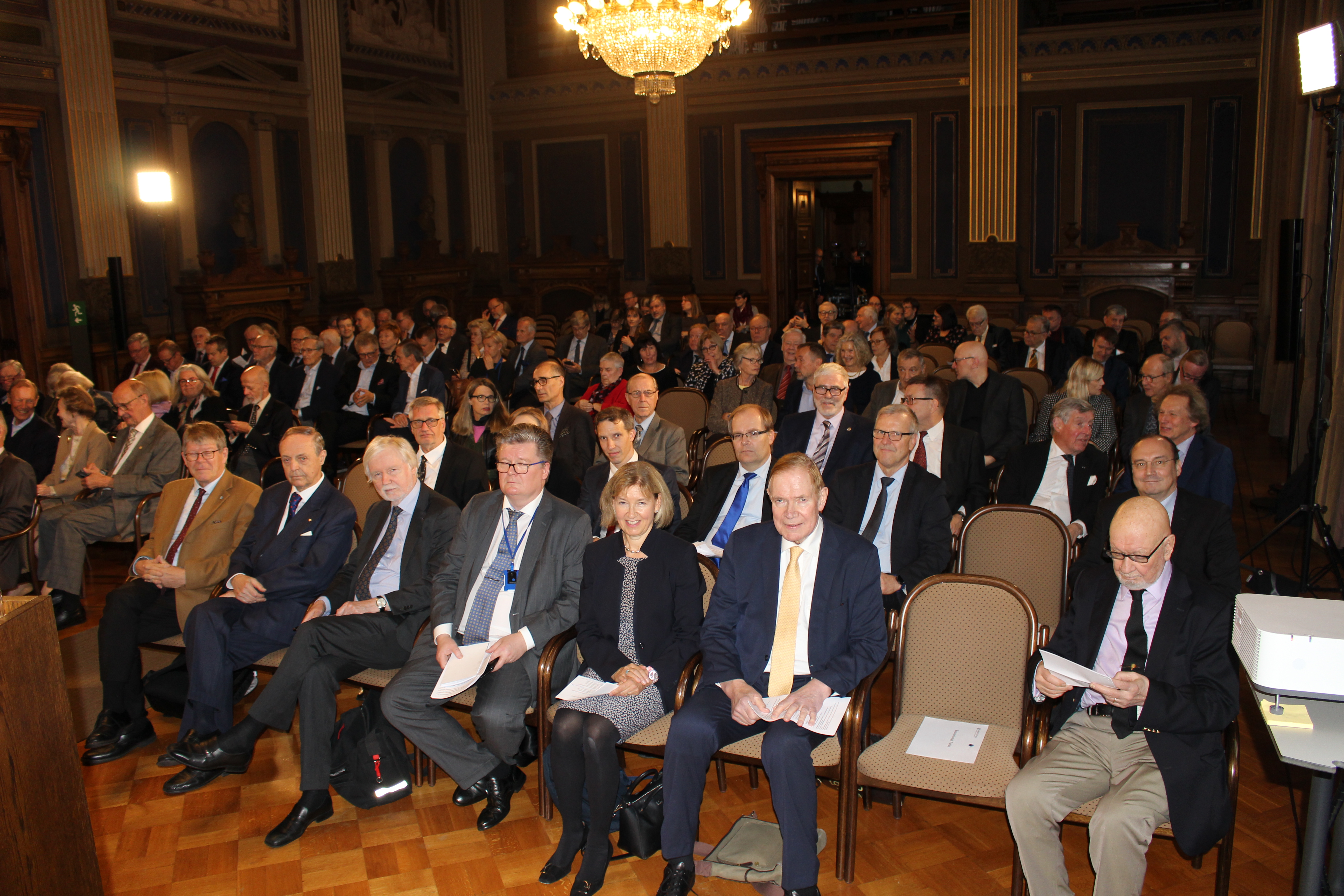 A large audience seated in the ornamental hall.